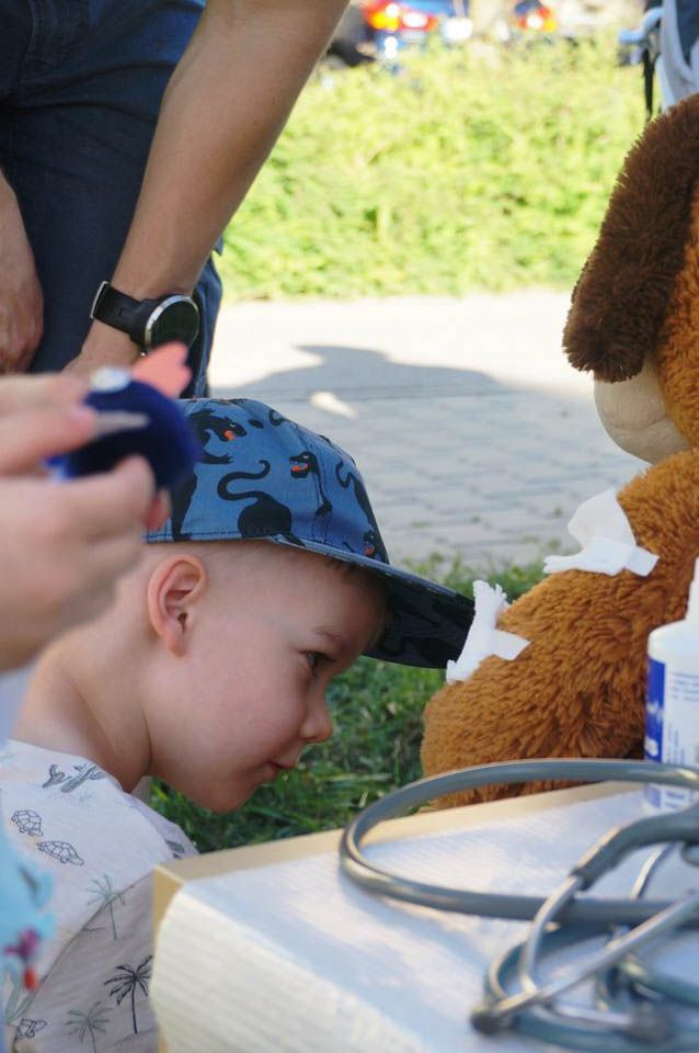 Chłopczyk z zainteresowaniem ogląda opatrunki na futrze pluszaka-misia w polowym szpitalu misia Eskulapka podczas Czerwcówki 2019 na Siekierkach