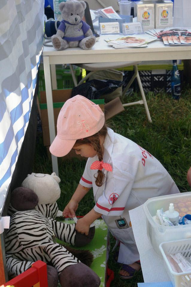 Mała dziewczynka-pediatra nakleja plaster na nogę chorej zebry-pluszaka podczas festynu na Siekierkach w Warszawie